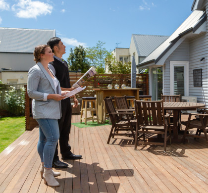 Two people standing outside a house for sale with a property magazine and checklist in hand