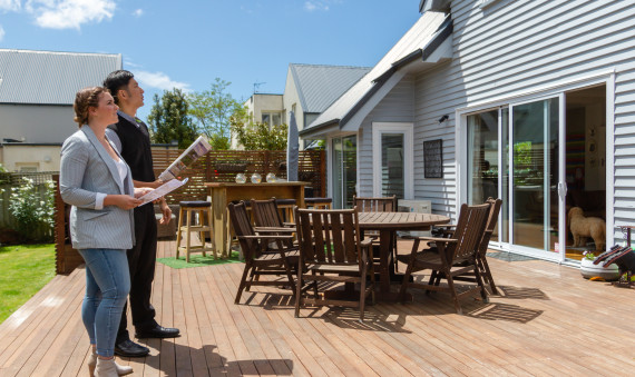 Two people standing outside a house for sale with a property magazine and checklist in hand