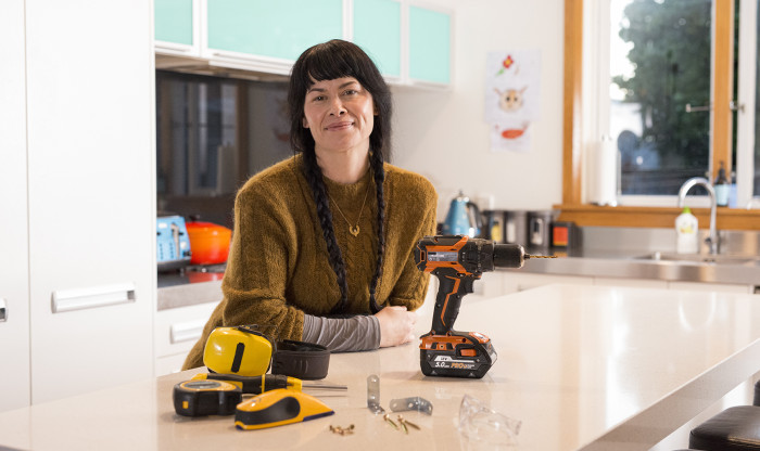 Person leaning against kitchen bench with a screwdriver and tools