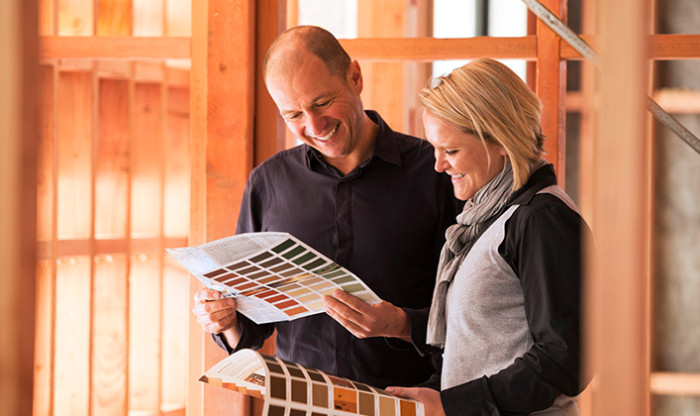 Two people standing inside the timber frame of their new home, picking colours to paint the walls