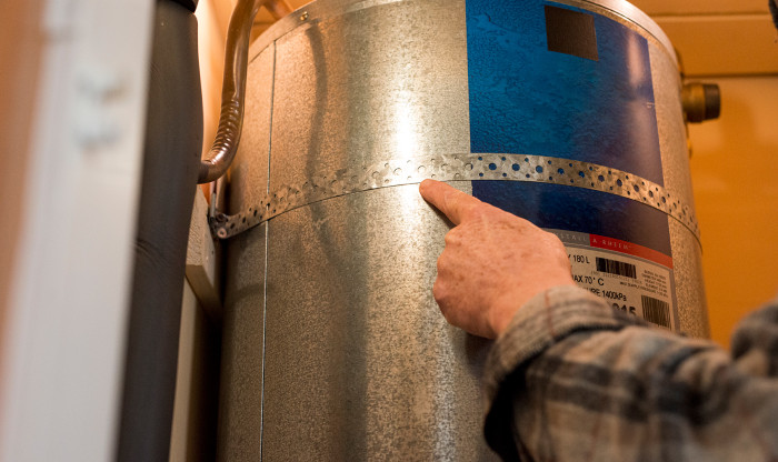 Person pointing to the straps securing a hot water cylinder