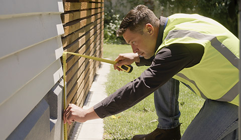 A man measuring house foundations as part of an inspection