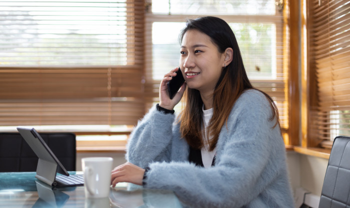 Woman sits at dining room table with her laptop open talking on the phone