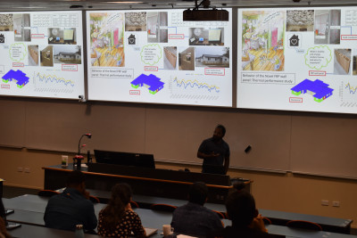 Lecturer stands in front of presentation in a lecture theatre 