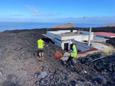 Two researchers walk on lava flows surrounding a building