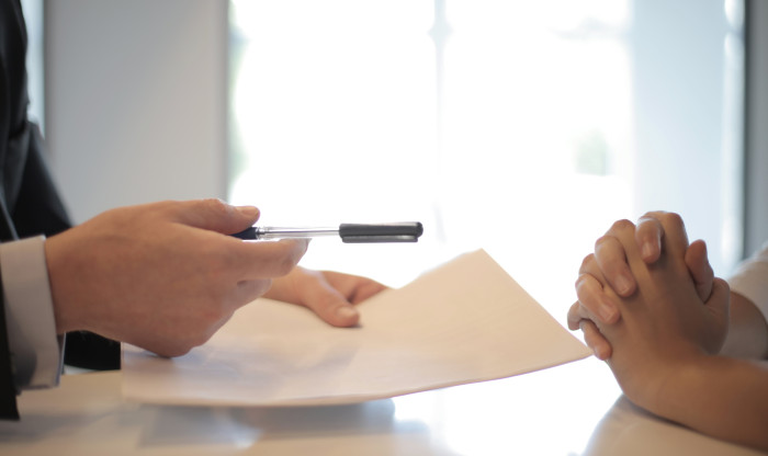 close up on hands giving a piece of paper and a pen to another pair of hands