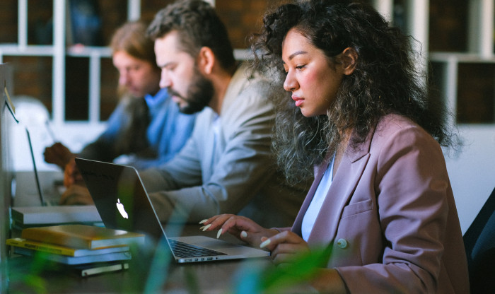 Three people are working at a desk on laptops